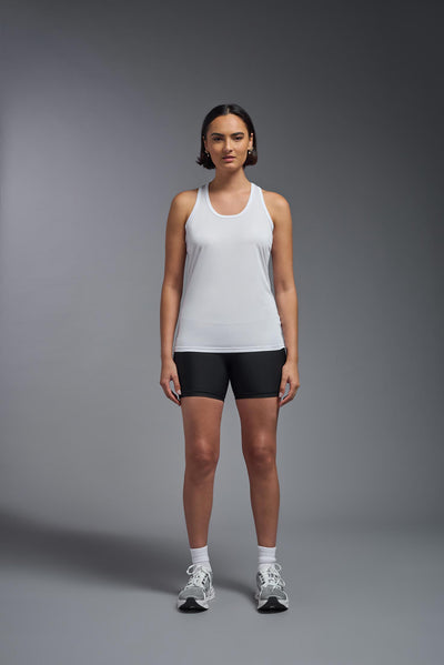A female model with brown short hair on a gray background, wearing the Women's DrImax Endurance Racerback Tank in the color white from a full body front view. This tank is made in the USA and is quick-drying and moisture-wicking. #color_white