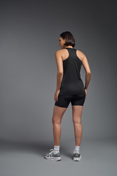 A female model with brown short hair on a gray background, wearing the Women's Drimax Endurance Racerback Tank in the color black from a full body back view. This tank is made in the USA and is quick-drying and moisture-wicking. #color_black