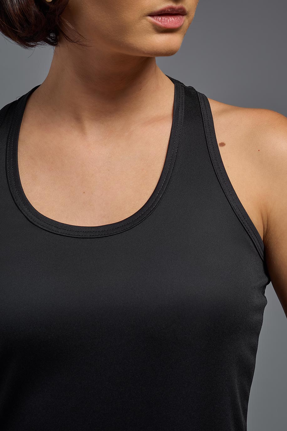 A female model with brown short hair on a gray background, wearing the Women's Drimax Endurance Racerback Tank in the color black from a full body collar view. This tank is made in the USA and is quick-drying and moisture-wicking. #color_black