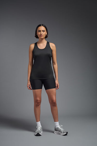 A female model with brown short hair on a gray background, wearing the Women's Drimax Endurance Racerback Tank in the color black from a full body front view. This tank is made in the USA and is quick-drying and moisture-wicking. #color_black