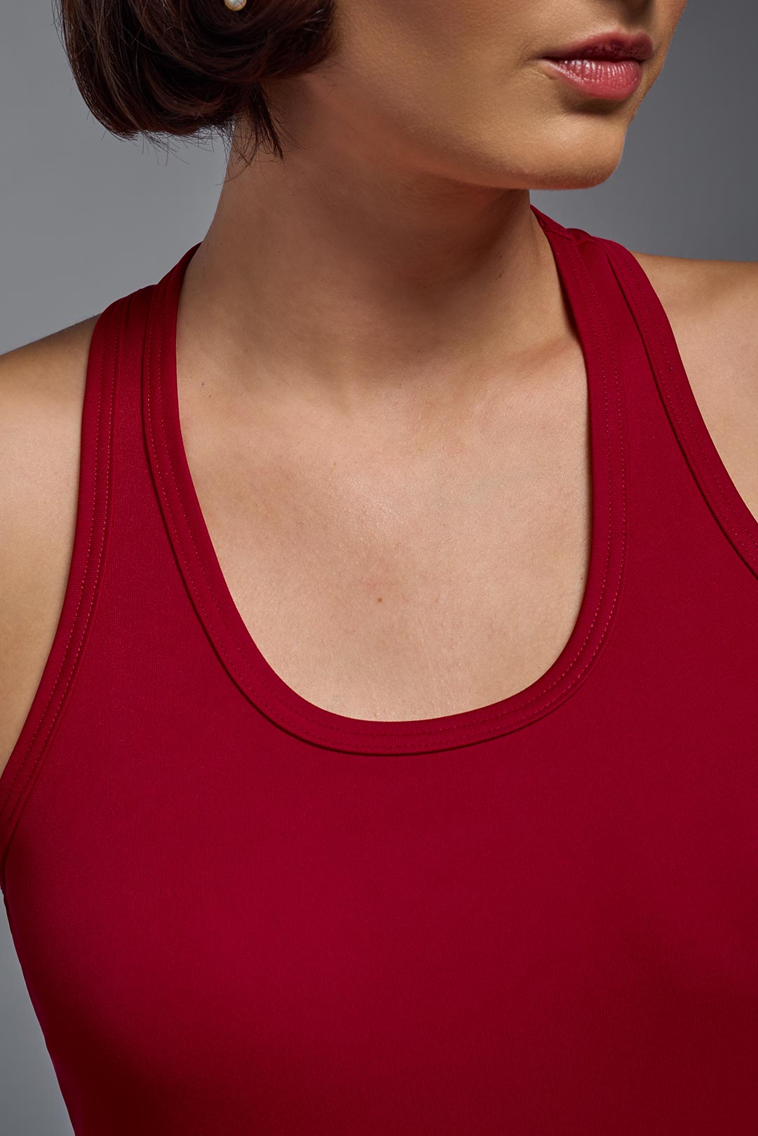 A female model with brown short hair on a gray background, wearing the Women's Drimax Endurance Racerback Tank in the color true red from a close up collar front view. This tank is made in the USA and is quick-drying and moisture-wicking. #color_true-red