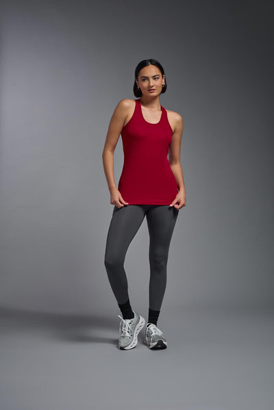 A female model with brown short hair on a gray background, wearing the Women's Drimax Endurance Racerback Tank in the color true red from a full body front view. This tank is made in the USA and is quick-drying and moisture-wicking. #color_true-red