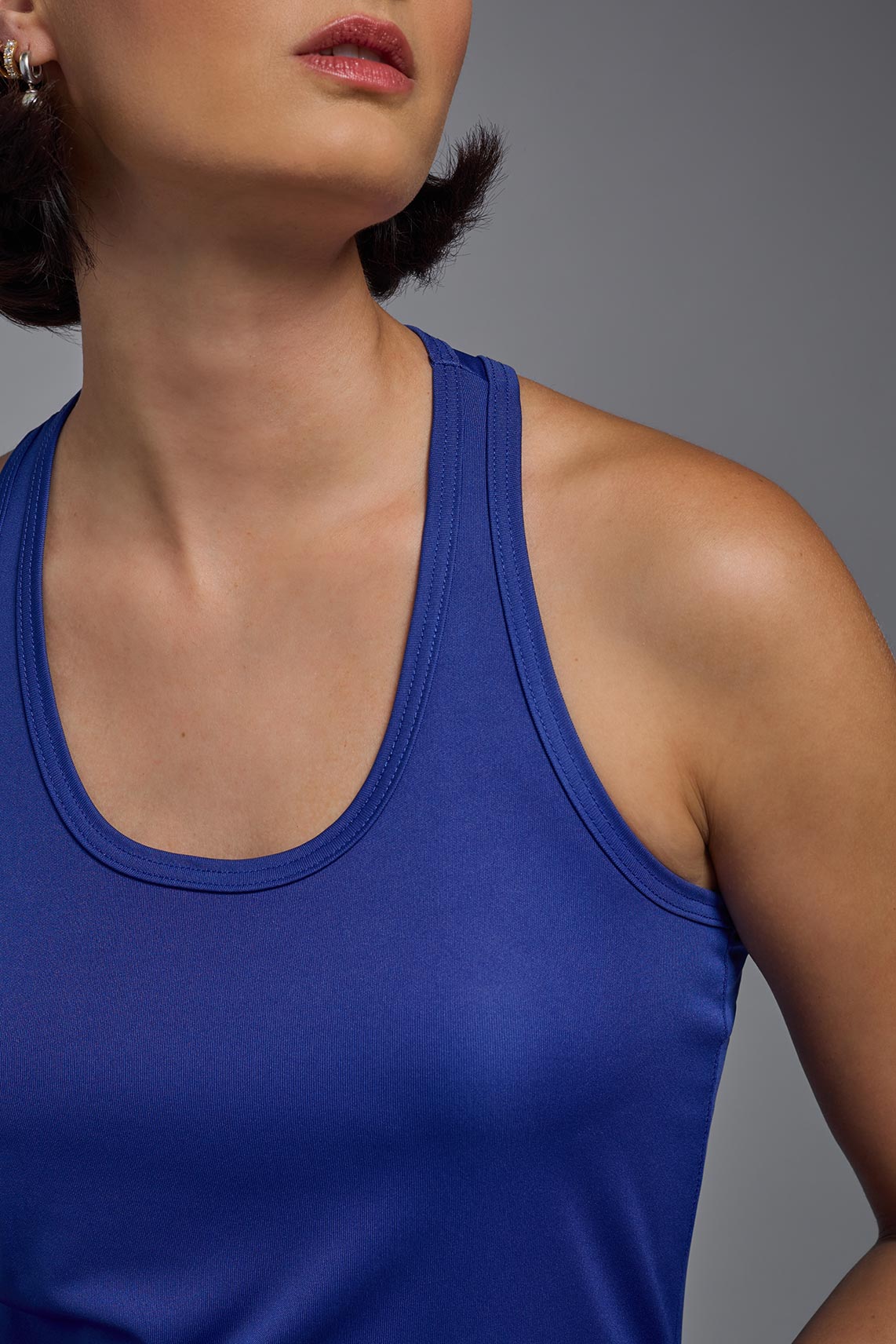 A female model with brown short hair on a gray background, wearing the Women's Drimax Endurance Racerback Tank in the color royal blue from a collar closeup view. This tank is made in the USA and is quick-drying and moisture-wicking. #color_royal-blue