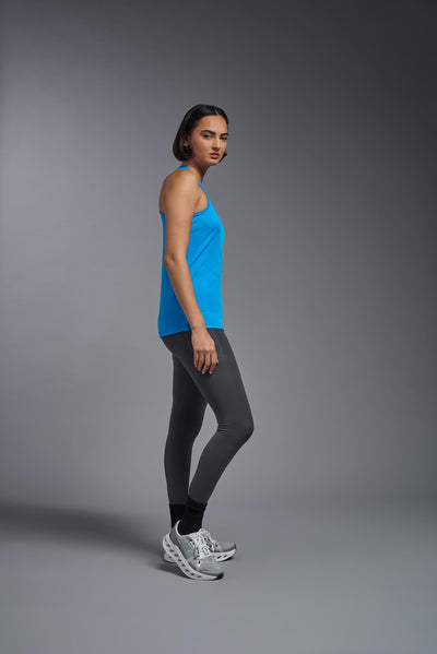 A female model with brown short hair on a gray background, wearing the Women's Drimax Endurance Racerback Tank in the color safety blue from a full body side view. This tank is made in the USA and is quick-drying and moisture-wicking. #color_safety-blue
