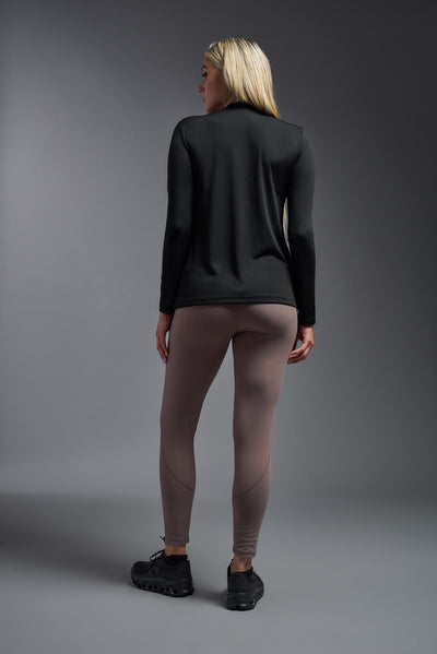 A blonde female model with long straight hair on a gray background, wearing the Women's DriMax™ V-neck Long Sleeve Expert Tee in the color black from a full body back view. This shirt is made in the USA and is quick-drying and moisture-wicking. #color_black