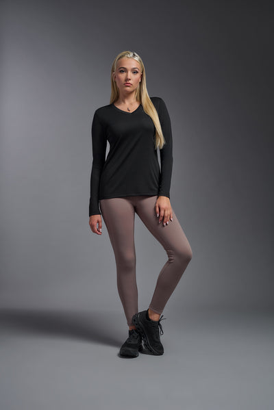 A blonde female model with long straight hair on a gray background, wearing the Women's DriMax™ V-neck Long Sleeve Expert Tee in the color black from a full body front view. This shirt is made in the USA and is quick-drying and moisture-wicking. #color_black