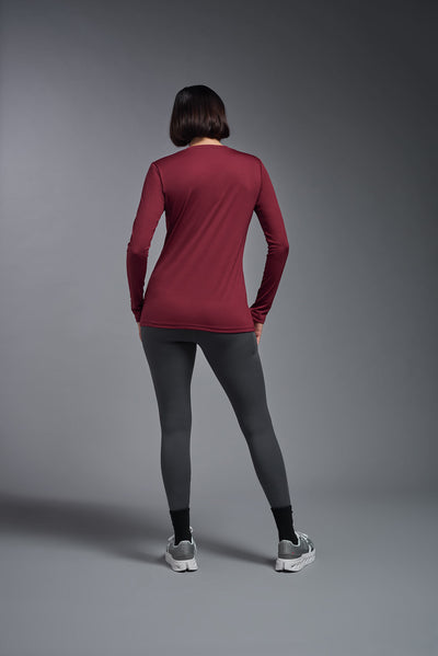 A female model with short brown hair on a gray background, wearing the Women's DriMax™ V-neck Long Sleeve Expert Tee in the color cardinal from a full body back view. This shirt is made in the USA and is quick-drying and moisture-wicking. #color_cardinal