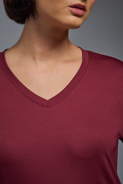 A female model with short brown hair on a gray background, wearing the Women's DriMax™ V-neck Long Sleeve Expert Tee in the color cardinal from a closeup collar front view. This shirt is made in the USA and is quick-drying and moisture-wicking. #color_cardinal