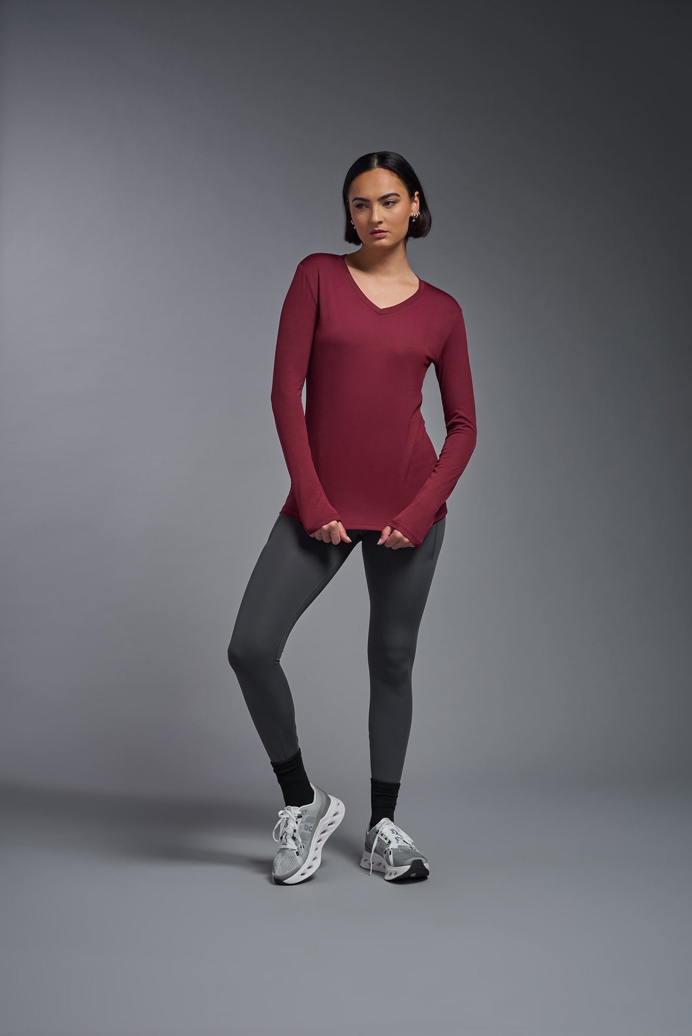 A female model with short brown hair on a gray background, wearing the Women's DriMax™ V-neck Long Sleeve Expert Tee in the color cardinal from a full body front view. This shirt is made in the USA and is quick-drying and moisture-wicking. #color_cardinal