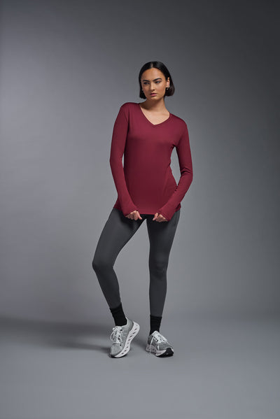 A female model with short brown hair on a gray background, wearing the Women's DriMax™ V-neck Long Sleeve Expert Tee in the color cardinal from a full body front view. This shirt is made in the USA and is quick-drying and moisture-wicking. #color_cardinal