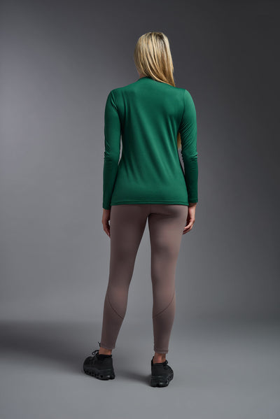 A blonde female model with long straight hair on a gray background, wearing the Women's DriMax™ V-neck Long Sleeve Expert Tee in the color forest green from a full body back view. This shirt is made in the USA and is quick-drying and moisture-wicking. #color_forest-green