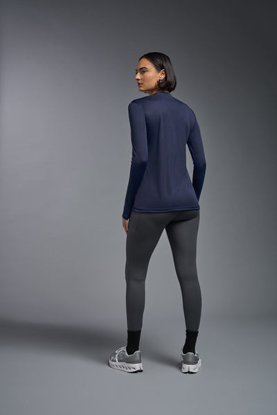 A female model with short brown hair on a gray background, wearing the Women's DriMax™ V-neck Long Sleeve Expert Tee in the color navy from a closeup collar back view. This shirt is made in the USA and is quick-drying and moisture-wicking. #color_navy
