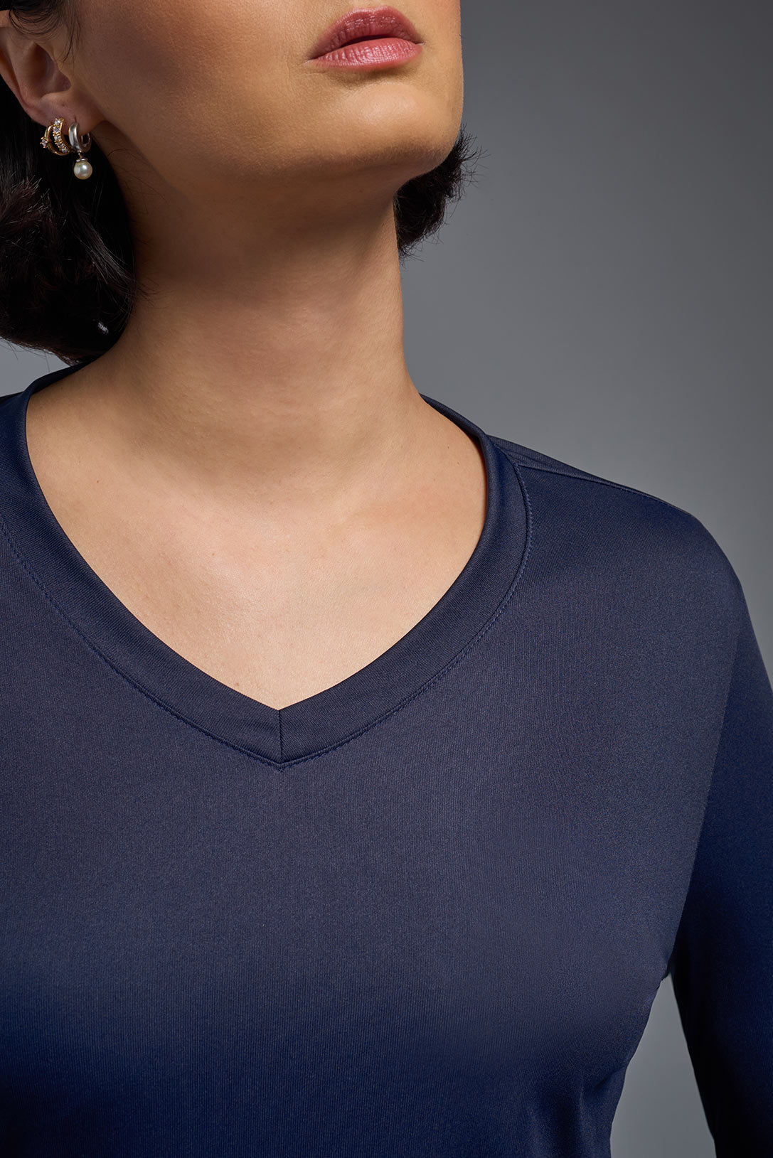 A female model with short brown hair on a gray background, wearing the Women's DriMax™ V-neck Long Sleeve Expert Tee in the color navy from a closeup collar front view. This shirt is made in the USA and is quick-drying and moisture-wicking. #color_navy