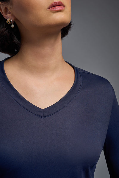 A female model with short brown hair on a gray background, wearing the Women's DriMax™ V-neck Long Sleeve Expert Tee in the color navy from a closeup collar front view. This shirt is made in the USA and is quick-drying and moisture-wicking. #color_navy