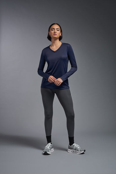 A female model with short brown hair on a gray background, wearing the Women's DriMax™ V-neck Long Sleeve Expert Tee in the color navy from a full body front view. This shirt is made in the USA and is quick-drying and moisture-wicking. #color_navy