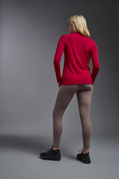 A blonde female model with long straight hair on a gray background, wearing the Women's DriMax™ V-neck Long Sleeve Expert Tee in the color red from a full body back view. This shirt is made in the USA and is quick-drying and moisture-wicking. #color_red