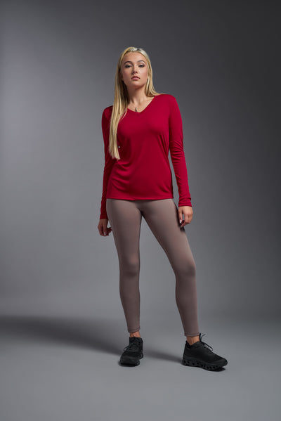 A blonde female model with long straight hair on a gray background, wearing the Women's DriMax™ V-neck Long Sleeve Expert Tee in the color true red from a full body front view. This shirt is made in the USA and is quick-drying and moisture-wicking. #color_red