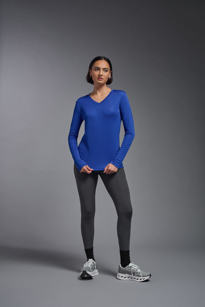 A female model with short brown hair on a gray background, wearing the Women's DriMax™ V-neck Long Sleeve Expert Tee in the color royal blue from a full body front view. This shirt is made in the USA and is quick-drying and moisture-wicking. #color_royal-blue