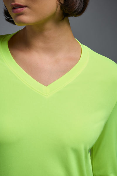 A female model with short brown hair on a gray background, wearing the Women's DriMax™ V-neck Long Sleeve Expert Tee in the color safety yellow from a closeup collar front view. This shirt is made in the USA and is quick-drying and moisture-wicking. #color_safety-yellow