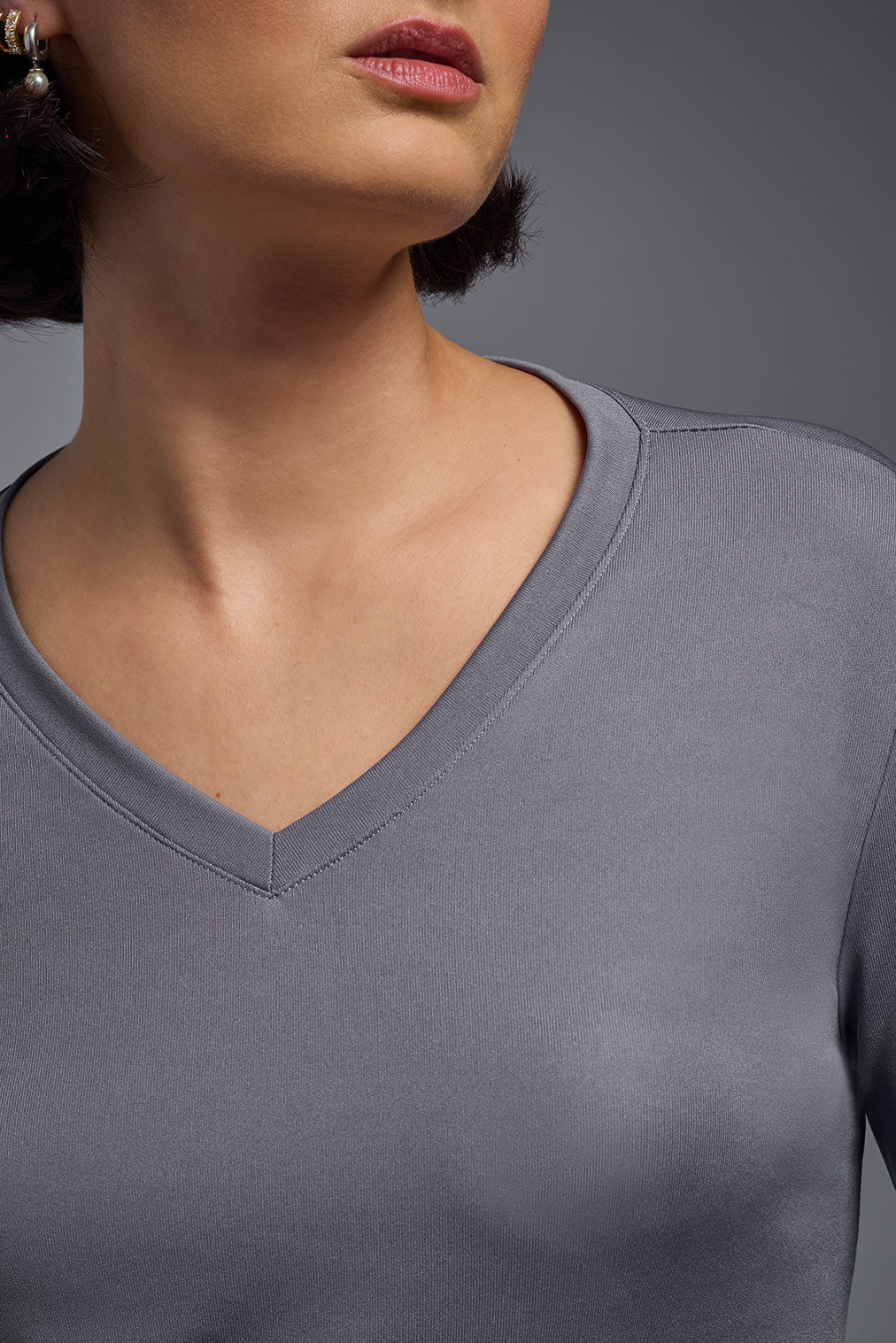 A female model with short brown hair on a gray background, wearing the Women's DriMax™ V-neck Long Sleeve Expert Tee in the color steel gray from a closeup collar front view. This shirt is made in the USA and is quick-drying and moisture-wicking. #color_steel