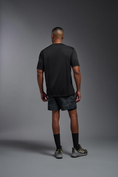 An African American male model with a beard on a gray background, wearing the Men's DriMax Expert Tee Shirt in the color black from a full body back view. This shirt is made in the USA and is quick-drying and moisture-wicking. #color_black