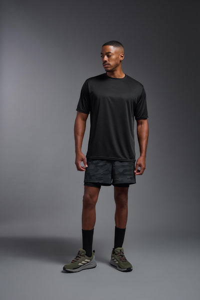 An African American male model with a beard on a gray background, wearing the Men's DriMax Expert Tee Shirt in the color black from a full body front view. This shirt is made in the USA and is quick-drying and moisture-wicking. #color_black