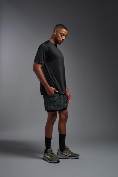 An African American male model with a beard on a gray background, wearing the Men's DriMax Expert Tee Shirt in the color black from a full body side view. This shirt is made in the USA and is quick-drying and moisture-wicking. #color_black