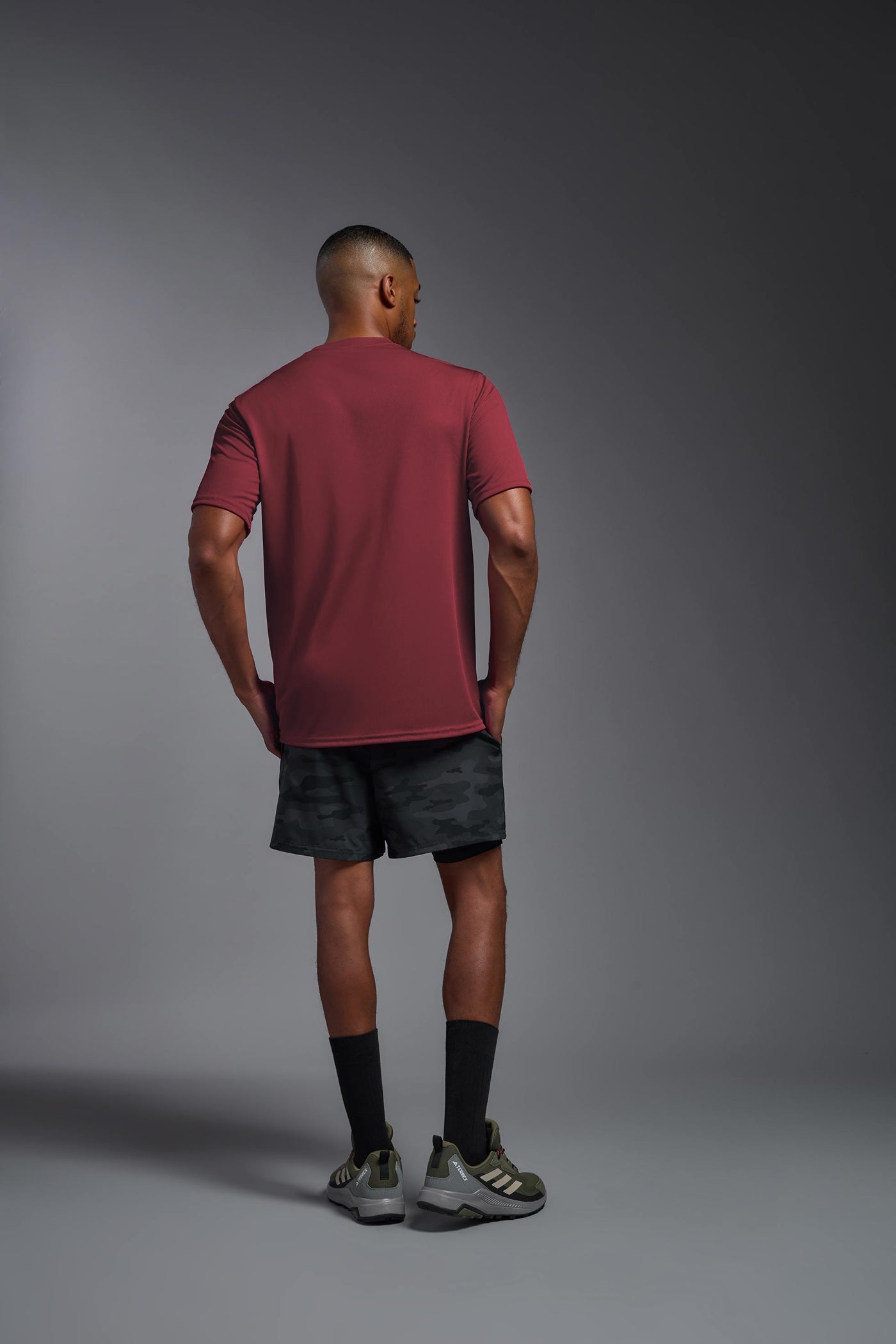 An African American male model with a beard on a gray background, wearing the Men's DriMax Expert Tee Shirt in the color cardinal from a full body back view. This shirt is made in the USA and is quick-drying and moisture-wicking. #color_cardinal