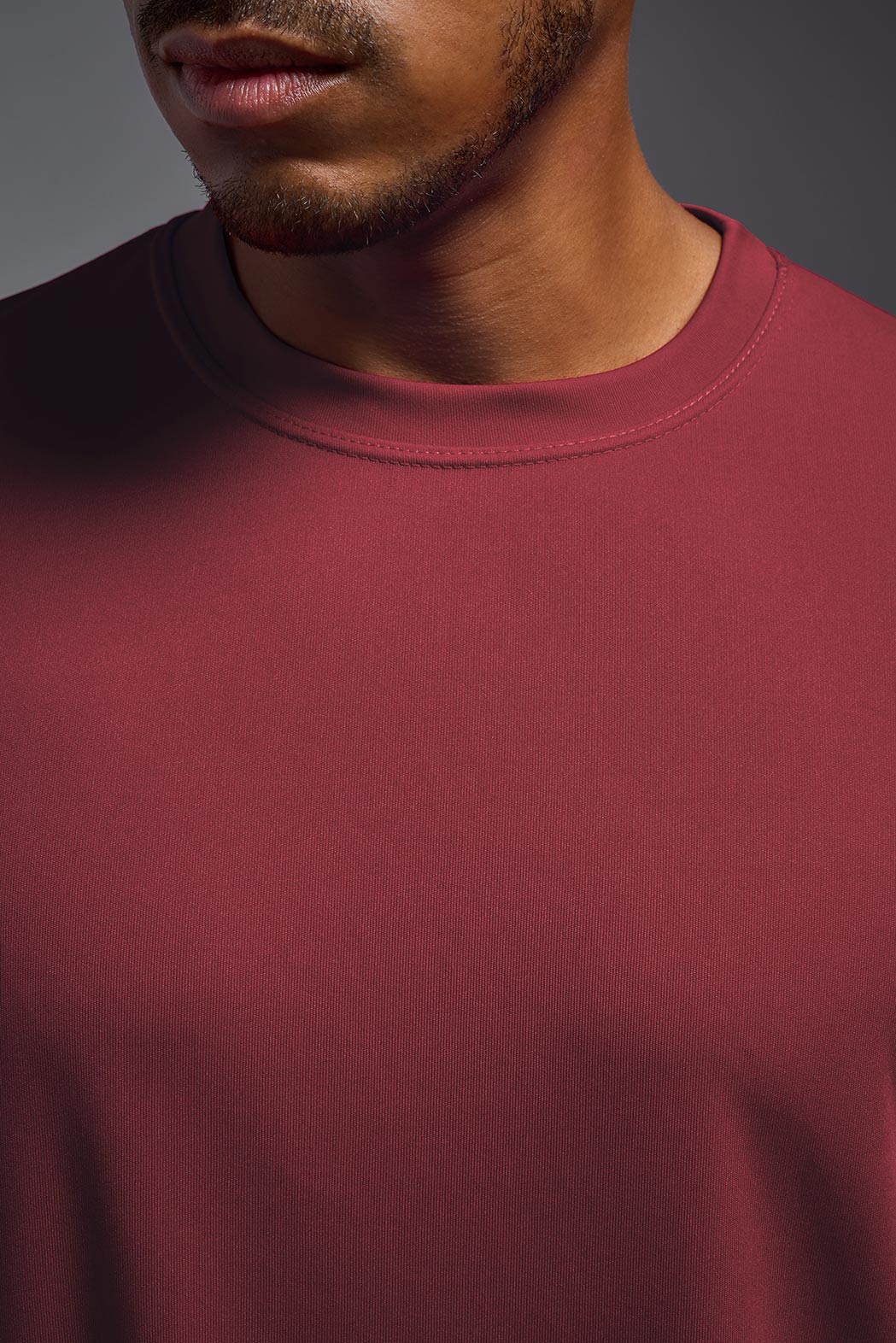 An African American male model with a beard on a gray background, wearing the Men's DriMax Expert Tee Shirt in the color cardinal from a collar closeup front view. This shirt is made in the USA and is quick-drying and moisture-wicking. #color_cardinal