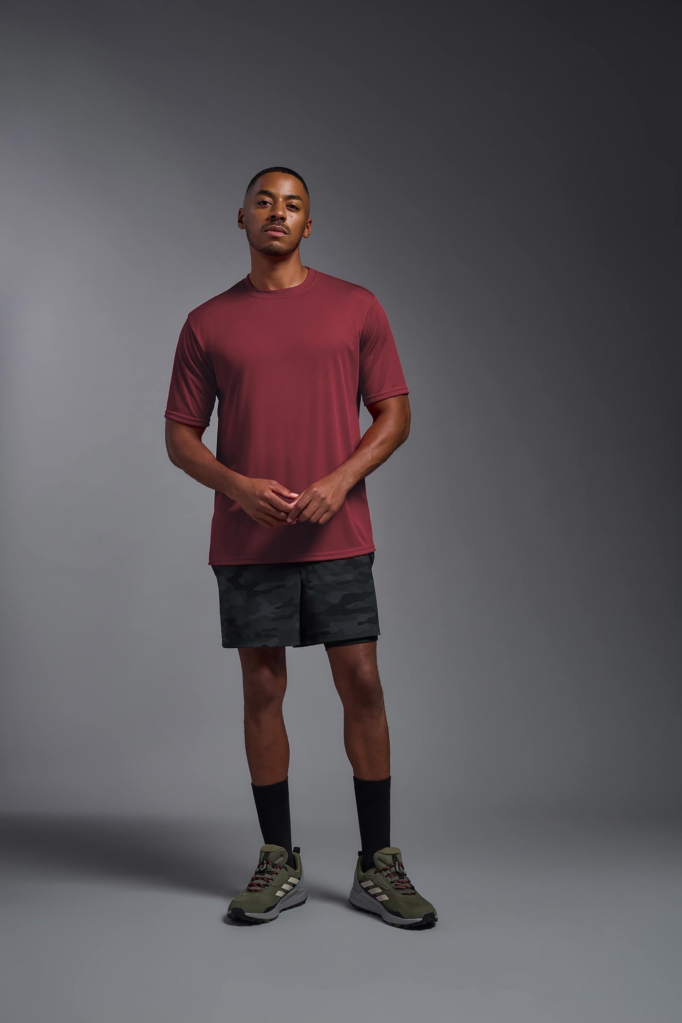 An African American male model with a beard on a gray background, wearing the Men's DriMax Expert Tee Shirt in the color cardinal from a full body front view. This shirt is made in the USA and is quick-drying and moisture-wicking. #color_cardinal
