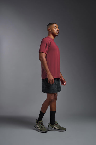 An African American male model with a beard on a gray background, wearing the Men's DriMax Expert Tee Shirt in the color cardinal from a full body side view. This shirt is made in the USA and is quick-drying and moisture-wicking. #color_cardinal