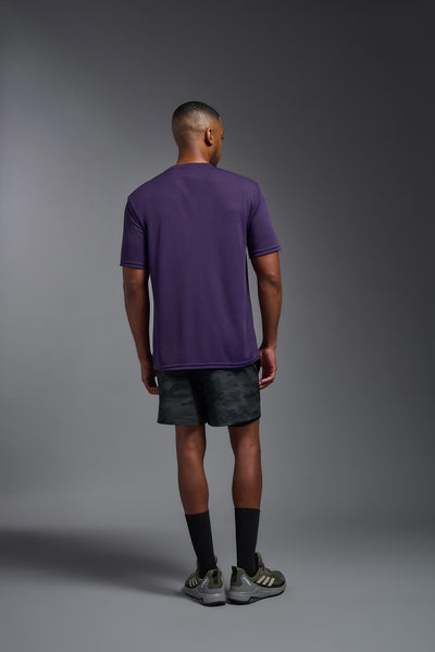 An African American male model with a beard on a gray background, wearing the Men's DriMax Expert Tee Shirt in the color dark purple from a full body back view. This shirt is made in the USA and is quick-drying and moisture-wicking. #color_dark-purple