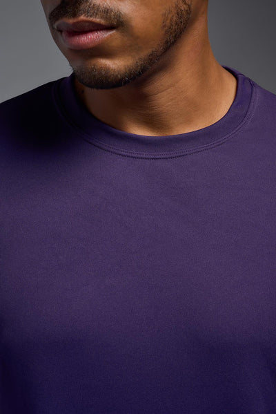 An African American male model with a beard on a gray background, wearing the Men's DriMax Expert Tee Shirt in the color dark purple from a full body collar close-up view. This shirt is made in the USA and is quick-drying and moisture-wicking. #color_dark-purple