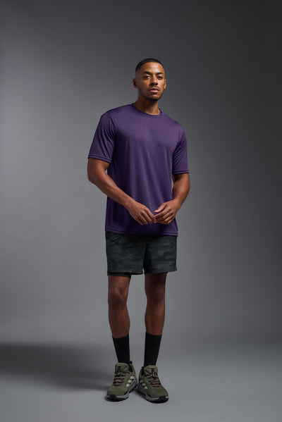 An African American male model with a beard on a gray background, wearing the Men's DriMax Expert Tee Shirt in the color dark purple from a full body front view. This shirt is made in the USA and is quick-drying and moisture-wicking. #color_dark-purple