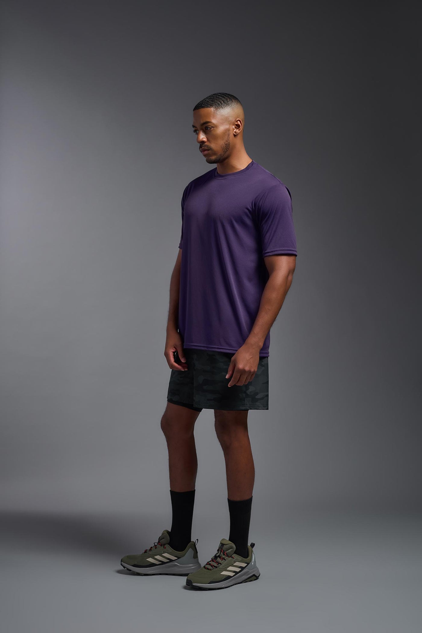An African American male model with a beard on a gray background, wearing the Men's DriMax Expert Tee Shirt in the color dark purple from a full body side view. This shirt is made in the USA and is quick-drying and moisture-wicking. #color_dark-purple