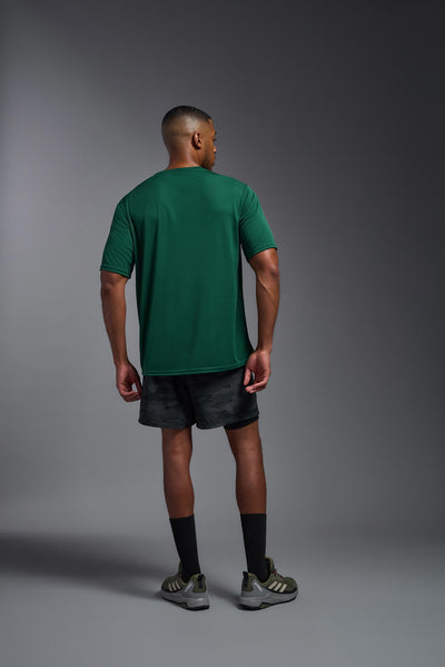 An African American male model with a beard on a gray background, wearing the Men's DriMax Expert Tee Shirt in the color forest green from a full body back view. This shirt is made in the USA and is quick-drying and moisture-wicking. #color_forest-green