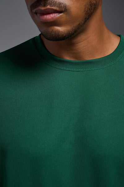 An African American male model with a beard on a gray background, wearing the Men's DriMax Expert Tee Shirt in the color forest green from a full body collar close-up view. This shirt is made in the USA and is quick-drying and moisture-wicking. #color_forest-green