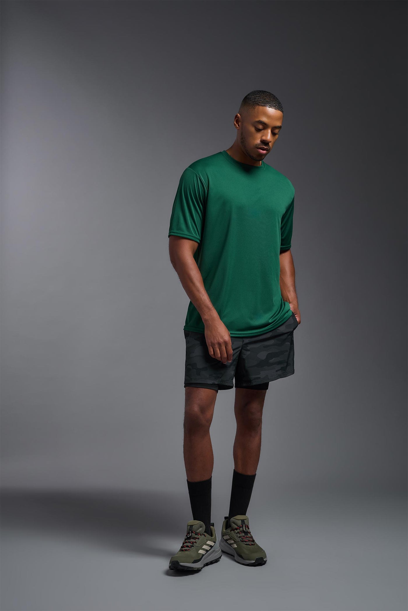 An African American male model with a beard on a gray background, wearing the Men's DriMax Expert Tee Shirt in the color forest green from a full body view. This shirt is made in the USA and is quick-drying and moisture-wicking. #color_forest-green