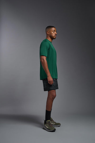 An African American male model with a beard on a gray background, wearing the Men's DriMax Expert Tee Shirt in the color dark purple from a full body side view. This shirt is made in the USA and is quick-drying and moisture-wicking. #color_dark-purple