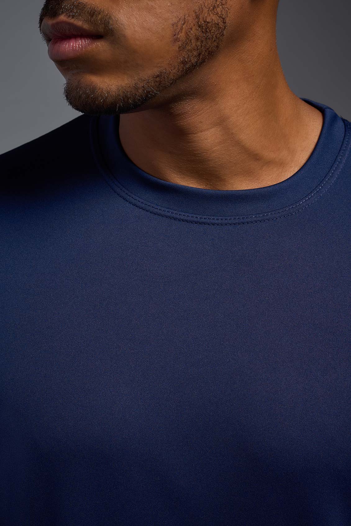 An African American male model with a beard on a gray background, wearing the Men's DriMax Expert Tee Shirt in the color  navy from a close-up collar front view. This shirt is made in the USA and is quick-drying and moisture-wicking. #color_navy