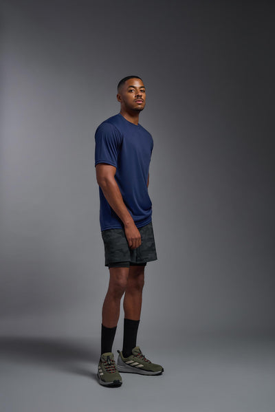 An African American male model with a beard on a gray background, wearing the Men's DriMax Expert Tee Shirt in the color  navy from a full body side view. This shirt is made in the USA and is quick-drying and moisture-wicking. #color_navy