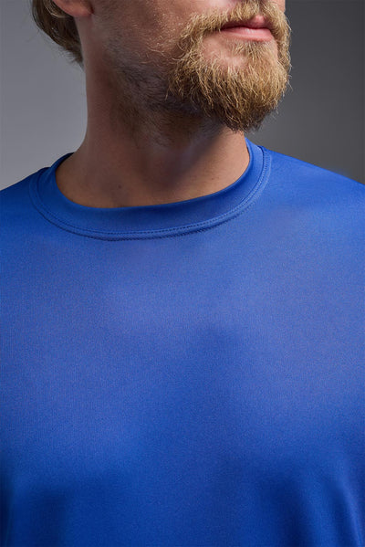 A blonde male model with a beard on a gray background, wearing the Men's DriMax Expert Tee Shirt in the color royal blue from a close-up collar view. This shirt is made in the USA and is quick-drying and moisture-wicking. #color_royal-blue