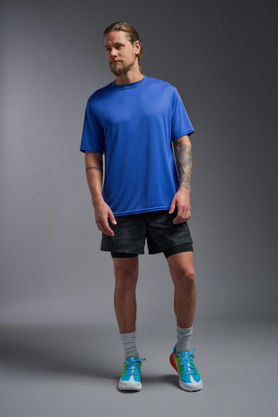 A blonde male model with a beard on a gray background, wearing the Men's DriMax Expert Tee Shirt in the color royal blue from a full body front view. This shirt is made in the USA and is quick-drying and moisture-wicking. #color_royal-blue