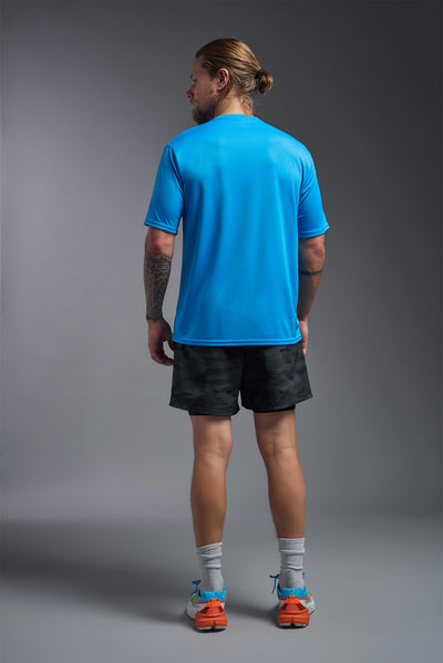 A blonde male model with a beard on a gray background, wearing the Men's DriMax shirt in the color safety blue from a back view. This shirt is made in the USA and is quick-drying and moisture-wicking. #color_safety-blue