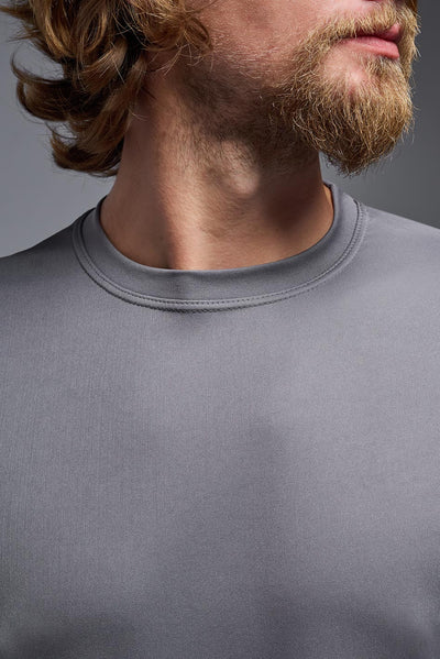 A blonde male model with a beard on a gray background, wearing the Men's DriMax Expert Tee Shirt in the color steel from a close-up collar view. This shirt is made in the USA and is quick-drying and moisture-wicking. #color_steel