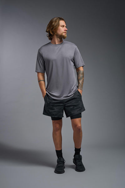 A blonde male model with a beard on a gray background, wearing the Men's DriMax Expert Tee Shirt in the color steel from a full body front view. This shirt is made in the USA and is quick-drying and moisture-wicking. #color_steel