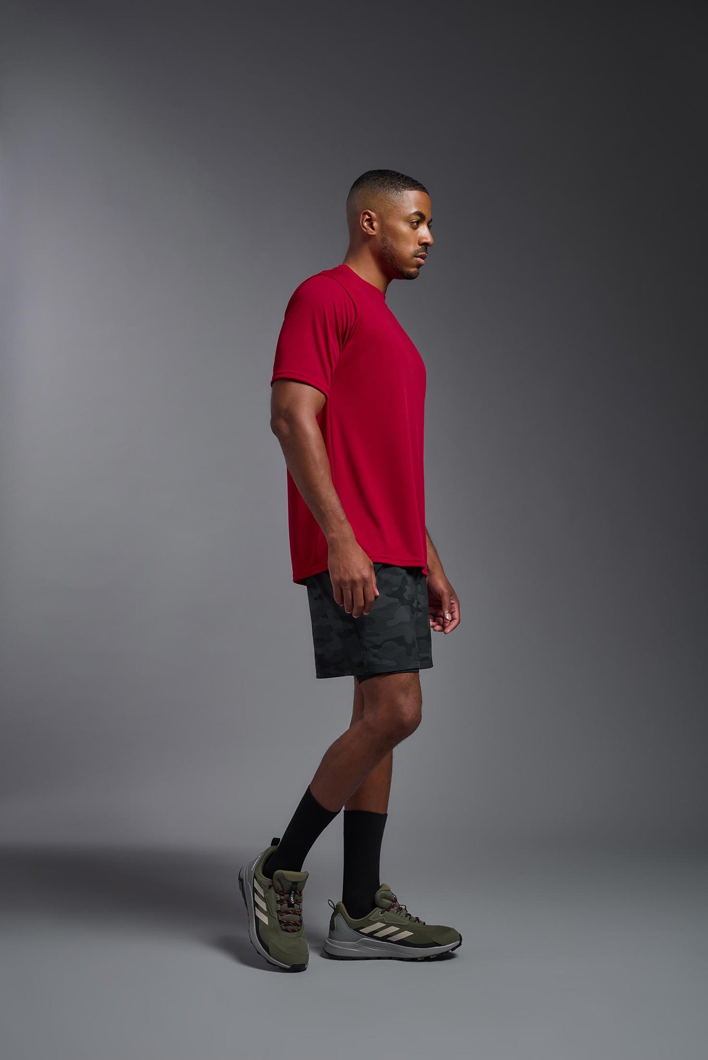 An African American male model with a beard on a gray background, wearing the Men's DriMax Expert Tee Shirt in the color true red from a full body side view. This shirt is made in the USA and is quick-drying and moisture-wicking. #color_true-red