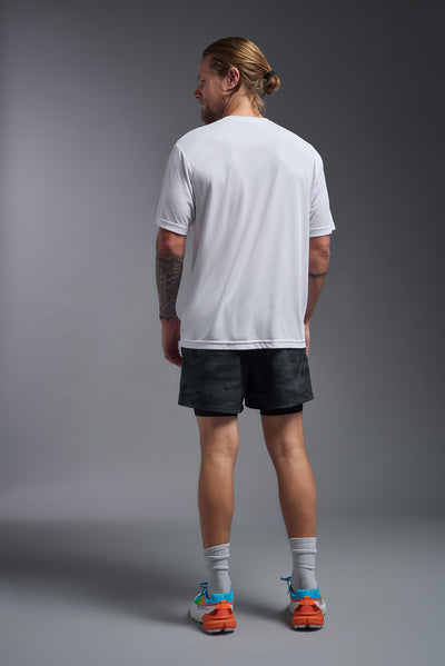 A blonde male model with a beard on a gray background, wearing the Men's DriMax Expert Tee Shirt in the color white from a full body back view. This shirt is made in the USA and is quick-drying and moisture-wicking. #color_white
