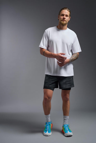 A blonde male model with a beard on a gray background, wearing the Men's DriMax Expert Tee Shirt in the color white from a full body front view. This shirt is made in the USA and is quick-drying and moisture-wicking. #color_white