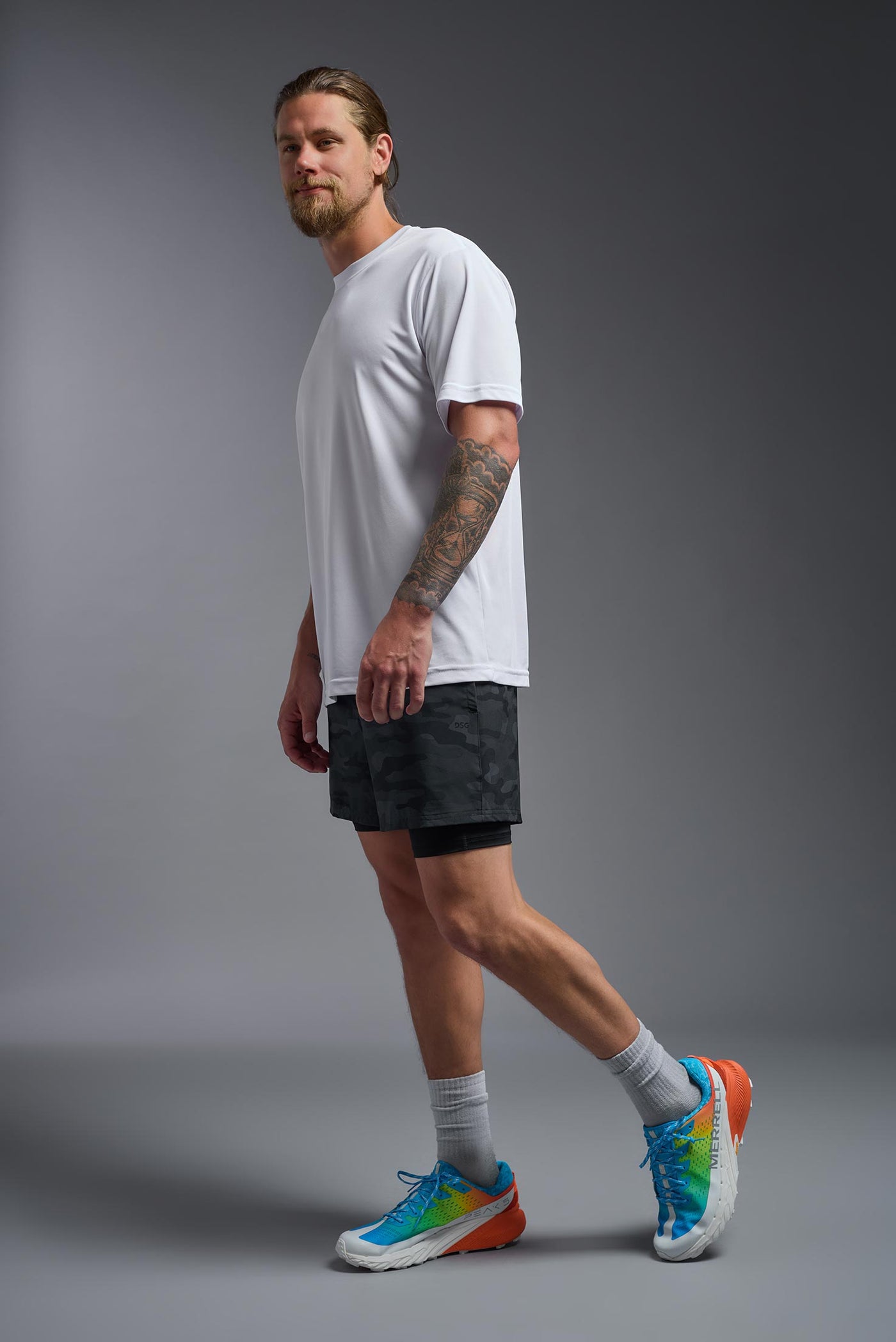 A blonde male model with a beard on a gray background, wearing the Men's DriMax Expert Tee Shirt in the color white from a full body side view. This shirt is made in the USA and is quick-drying and moisture-wicking. #color_white